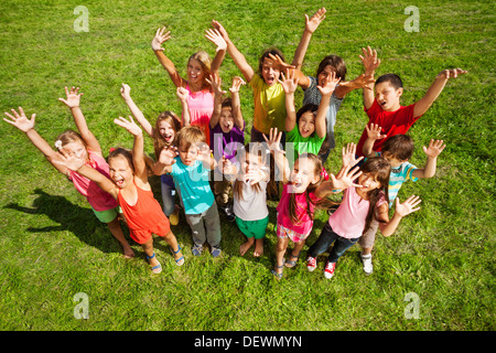 Große Gruppe von Kindern, jungen und Mädchen, mit aufgehobenen Händen etwa 10 Jahre alt, steht auf den grünen Rasen-Draufsicht Stockfoto