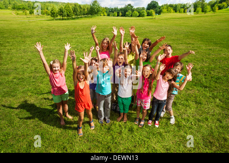 Große Gruppe von Happy Kids, Jungen und Mädchen, etwa 10 Jahre alt mit angehobenen Hände lächelnd und Schreien, stehend auf dem grünen Rasen Schießen von oben Stockfoto