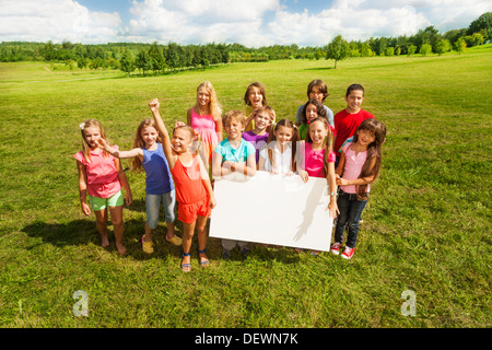 Gruppe von Kindern Holding leer Banner zeigt leere Plakette Vorstand am eigenen Text zu schreiben, steht auf der Wiese im Park Stockfoto