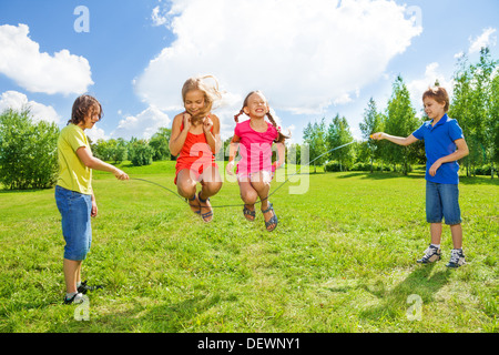 Zwei Mädchen mit Jungs drehen das Seil über das Seil springen Stockfoto