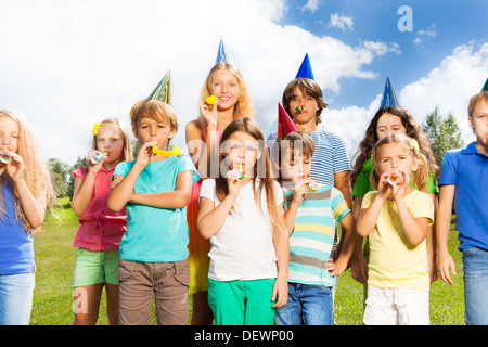 Große Gruppe von Kindern Alter 5 bis 11 außerhalb auf einem Geburtstag party bläst Krachmachern Hörner und Pfeifen verdreht Stockfoto