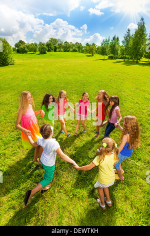 Große Gruppe der glückliche Mädchen spielen Roundelay und stehen im Kreis im Park auf dem grünen Rasen auf sonnigen Tag Draufsicht Stockfoto