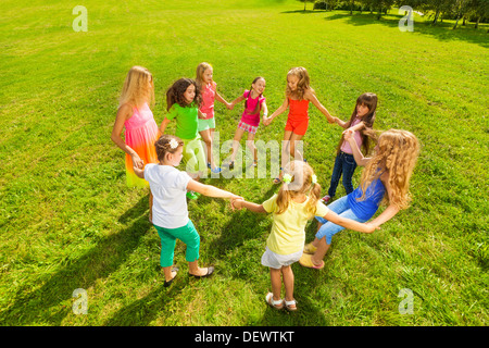 viele glückliche Mädchen spielen Roundelay und Tanz und stehen im Kreis im Park auf dem grünen Rasen an sonnigen Sommertag Stockfoto