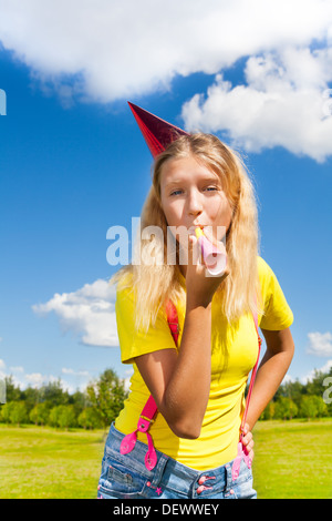 Wunderschöne kleine Mädchen bläst in krachmacher Horn und Geburtstagsfeier cap draußen stehen mit glücklichen Ausdruck auf sonnigen Sommertag Stockfoto