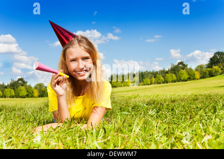 Portrait von jugendlich Mädchen mit krachmacher Horn und Geburtstagsfeier cap Verlegung außerhalb mit glücklichen Ausdruck auf sonnigen Sommertag Stockfoto