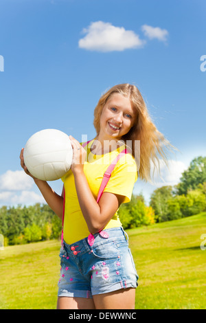 Süß und glücklich 13 Jahre altes Mädchen mit langen blonden Haaren stehen auf der Wiese mit dem Ball im Park an sonnigen Sommertag Stockfoto