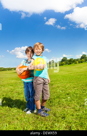 Zwei Geschwister jungen stehen mit Kugeln auf sonnigen Sommertag im Park stehen holding Stockfoto