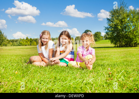 Drei glückliche Mädchen, Schwestern, sitzen auf der Wiese im Park zusammen Stockfoto