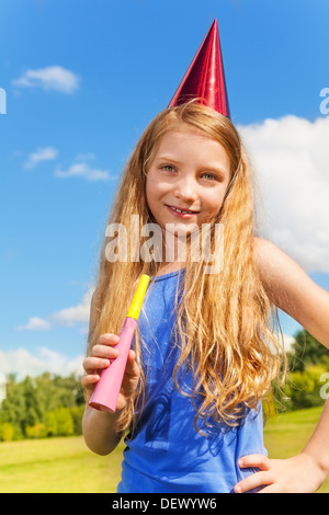 Wunderschönes kleines Mädchen mit Krachmacher Horn und Geburtstag party Mütze draußen mit glücklichen Ausdruck auf sonnigen Sommertag Stockfoto