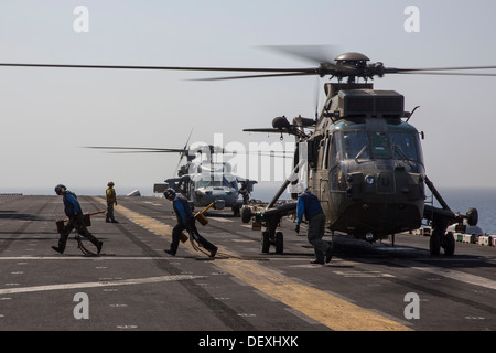 Matrosen entfernen Unterlegkeile und Ketten aus einem Hubschrauber der britischen Royal Navy Sea King MK 4 im Flugbetrieb auf dem Flugdeck Stockfoto