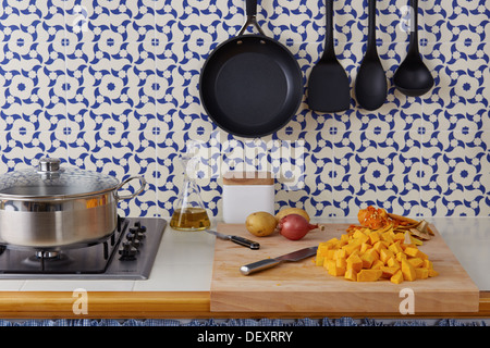 Schneiden Sie Gemüse wie Kürbis, Kartoffeln und Zwiebeln auf einem Schneidetisch in einem Vintage-geflieste Küche Stockfoto