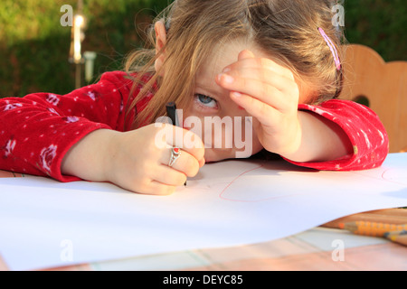 Kleines Mädchen, drei Jahre, Malen mit einem Stift auf einem weißen Blatt, an einem Tisch sitzen Stockfoto