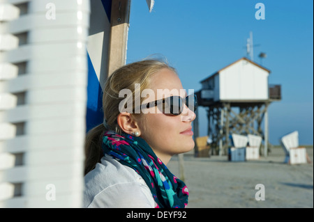 Junge Frau mit Sonnenbrille am Strand vor einem Haus auf Stelzen, St. Peter-Ording, Schleswig-Holstein, Deutschland Stockfoto