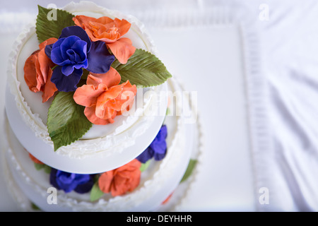 Drei Stufen Fondant gekräuselte weiße Hochzeitstorte dekoriert mit Orange und lila Gum paste Rosen und grünen Blätter, geschossen von oben Stockfoto