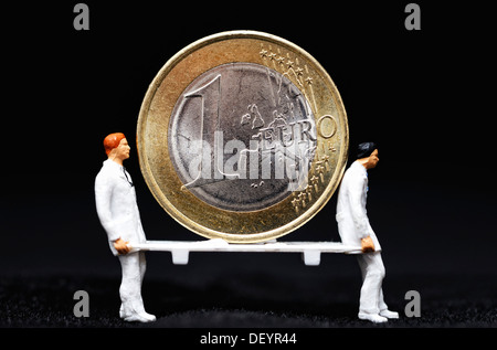 Ein-Euro-Münze als Patient auf einer Bahre, getragen von Miniaturfiguren, symbolisches Bild für die Euro-Krise Stockfoto