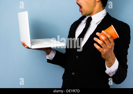 Junger Geschäftsmann ist schockiert über die Nachricht auf seinem Laptop und fast seinen Kaffee verschüttet Stockfoto