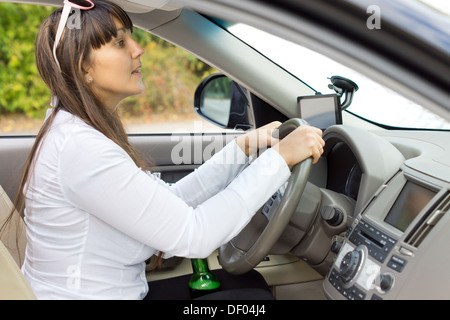 Betrunkene Fahrerin versucht, beurteilen ihre Distanzen umklammert ihre Flasche Schnaps zwischen ihre Schenkel und steigen bis über das Dashboard zu spähen. Stockfoto