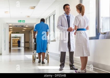 Asiatischen männlichen Arzt & Krankenschwester im Krankenhausflur mit afroamerikanischen schwarze Krankenschwester & senior Patientin im Rollstuhl Stockfoto