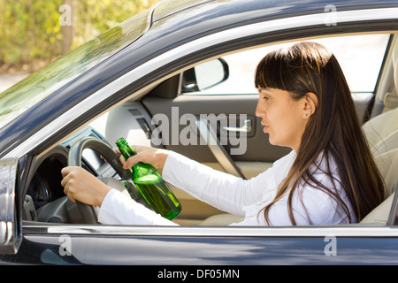 Gefährliche Fahrt mit einem betrunken und betrunkene Fahrerin schlaftrunken starrte auf ihr Lenkrad, wie sie fährt entlang eine Flasche Schnaps in der Hand halten. Stockfoto