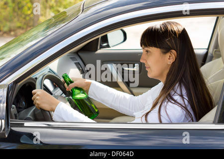Betrunken Frau Fahrer lächelnd wie sie mit einer Flasche Alkohol fest in einer Hand hielt fährt durch das Seitenfenster anzeigen Stockfoto