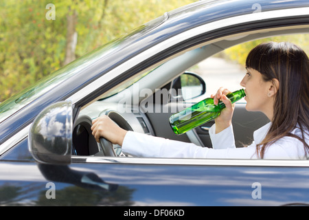 Betrunkene Fahrerin Alkohol direkt aus der Flasche zu trinken, wie sie ihr Auto auf der Straße, die eine Gefahr für andere darstellen steuert. Stockfoto