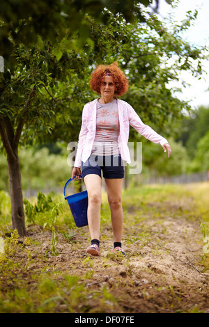 Bauer-Frau, die einen Eimer mit Dünger in einem Obstgarten, mit selektiven Fokus Stockfoto