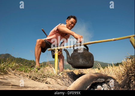Mann aus der Shan oder Thai Yai Volksgruppe, ist kochendes Wasser in eine eiserne Kessel, Soppong oder Pang Mapha, Nordthailand Stockfoto