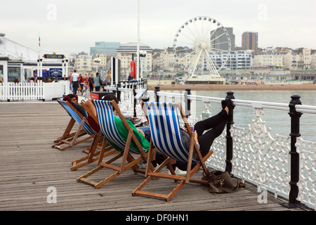 Jugendliche, die entspannend auf Liegestühlen am Pier von Brighton in East Sussex, England Stockfoto