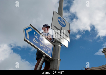 Ein Arbeiter Autobahnen installiert eine Busspur, Taxis und Zyklen nur unterzeichnen, plus ein "Nicht geeignet für LKWs" Warnschild am Laternenpfahl. Stockfoto