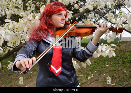 Ein junges Mädchen spielt die Violine im blühenden Garten. Sie ist ein Anime Kostüm und eine Perücke tragen. Stockfoto
