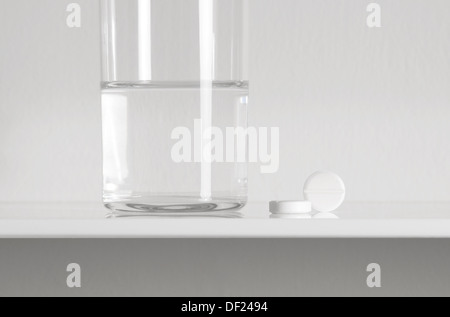 Aspirin-Tabletten und ein Glas Wasser auf weißen Regal Stockfoto