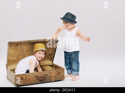 Kleines Kind versteckt sein älteren Bruder im Koffer Stockfoto