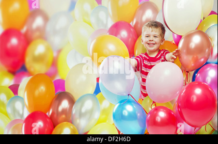 Lachender Junge spielt unter den bunten Luftballons Stockfoto