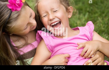 Niedliche Mädchen kitzeln ihre jüngere Schwester lachend Stockfoto