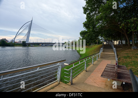 Gehweg und Bank neben See und Fluss mit Brücke im Hintergrund Stockfoto