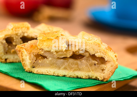 Halb Apfelkuchen mit Gitter Kruste auf grünen Serviette auf Holzbrett mit einer blauen Tasse Äpfel und Zimt-sticks in den Rücken Stockfoto