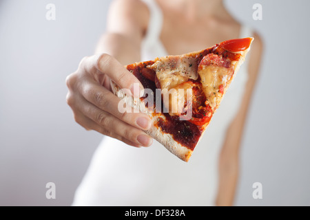 Frau hält Stück Pizza mit Tomaten, Speck, Salami und Käse. Holzbrett. Stockfoto