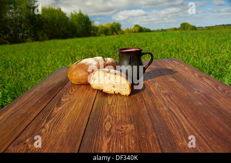 Selbstgebackenes Brot und Becher Milch auf einem Holztisch. Hintergrund blauer Himmel. Outdoor-Farm-Stil Stockfoto