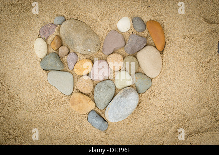 Kiesel, angeordnet in Form eines Herzens auf einem Sandstrand Stockfoto