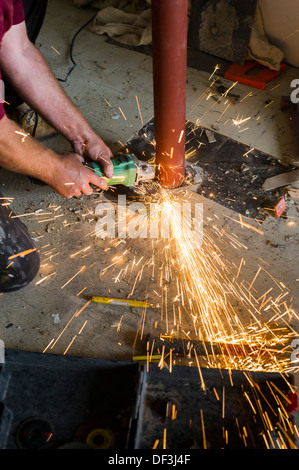 Ein Bauarbeiter mit einem Winkelschleifer, um ein Metallrohr zu schneiden. Stockfoto
