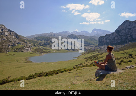 Junge Frau sitzt in Lotus Pose vor einem der Covadonga Seen, Asturien Stockfoto