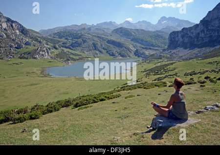 Junge Frau sitzt in Lotus Pose vor einem der Covadonga Seen, Asturien Stockfoto