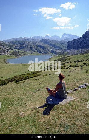 Junge Frau sitzt in Lotus Pose vor einem der Covadonga Seen, Asturien Stockfoto