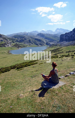 Junge Frau sitzt in Lotus Pose vor einem der Covadonga Seen, Asturien Stockfoto