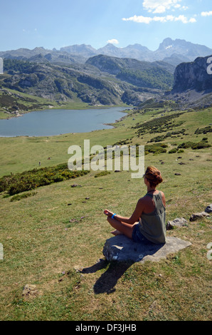 Junge Frau sitzt in Lotus Pose vor einem der Covadonga Seen, Asturien Stockfoto