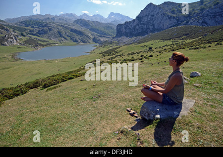 Junge Frau sitzt in Lotus Pose vor einem der Covadonga Seen, Asturien Stockfoto