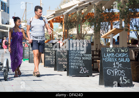 SANTORINI (THIRA), KYKLADEN, GRIECHENLAND. Vorbei an einer Taverne mit Wandtafeln Werbung Mahlzeit Angebote für zwei Urlauber. Stockfoto