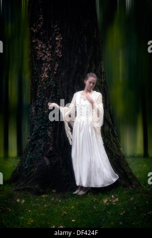 eine Mädchen in einem Zeitraum Kleid ist an einen Baum gelehnt. Stockfoto