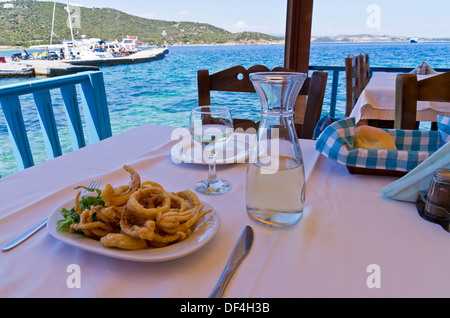 Gebratener Tintenfisch essen und trinken Weißwein in einen Schatten von einer typischen griechischen Taverne Stockfoto