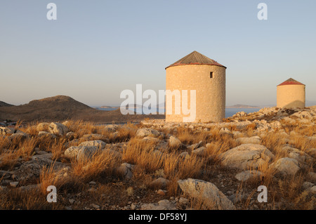 Alte Windmühlen stehen über Halki Chalki Hafen in den späten Abend Licht griechischen Inseln der Dodekanes Griechenland Stockfoto